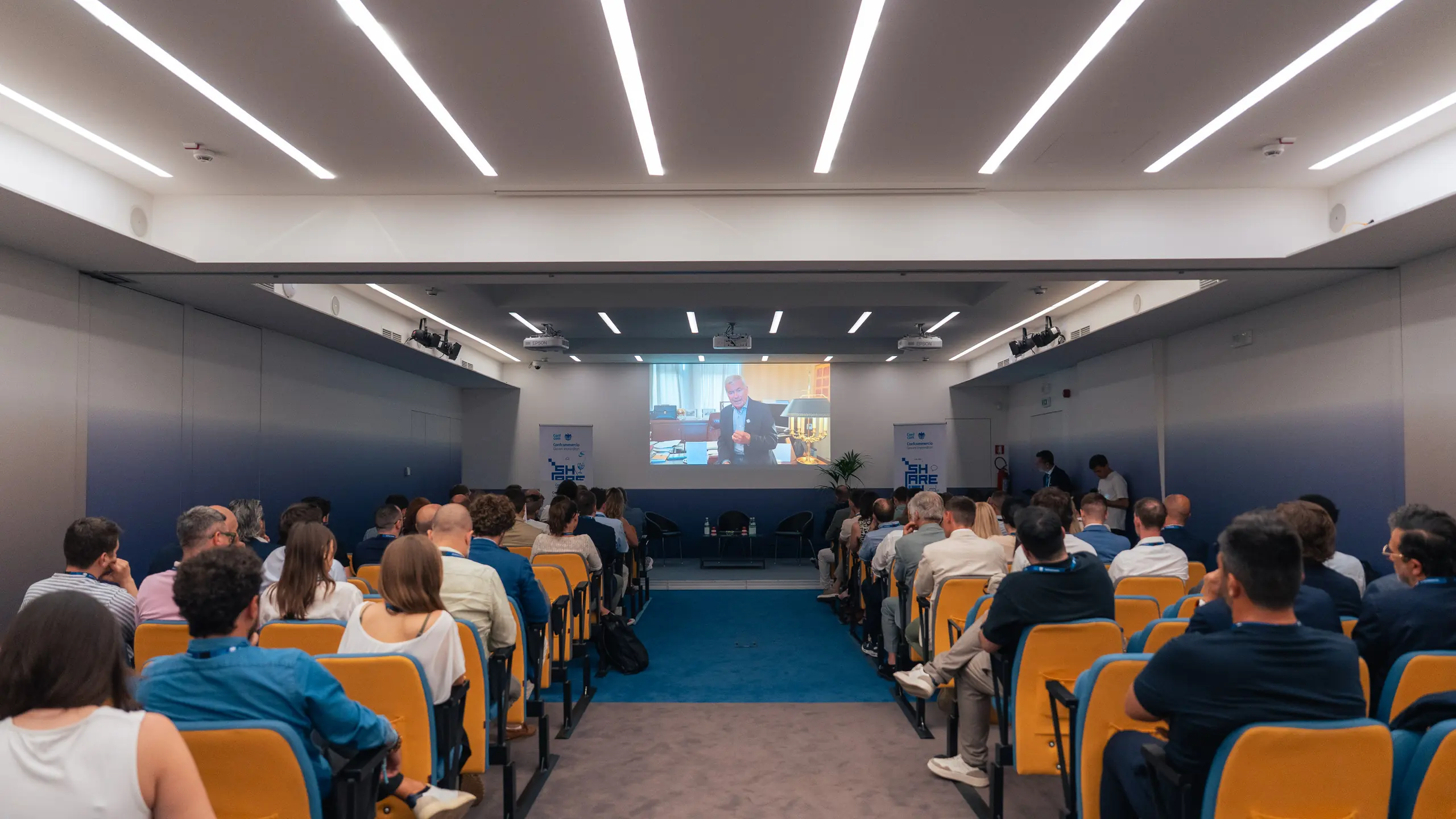 La sala di Share It a Padova vista dal fondo: il pubblico seduto in platea davanti allo schermo dei relatori